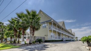 A two-story motel with a balcony on the second floor, palm trees in front, and a gravel driveway.