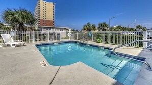 A swimming pool with a metal railing, lounge chairs, and a palm tree in the background.