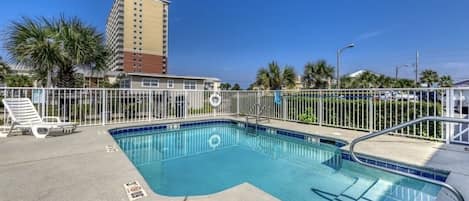 A swimming pool with a metal railing, lounge chairs, and a palm tree in the background.