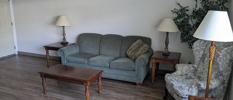 A living room with a sofa, two side tables, a coffee table, and a patterned armchair.