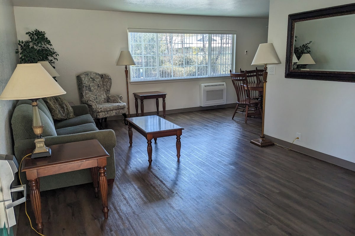 A living room with a sofa, two lamps, a coffee table, a chair, and a dining table.