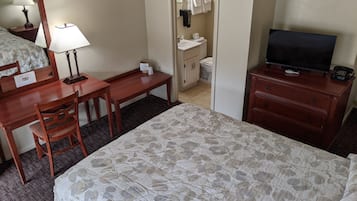 Habitación de hotel con cama, escritorio con silla, televisor, cómoda y baño visible a través de una puerta abierta.