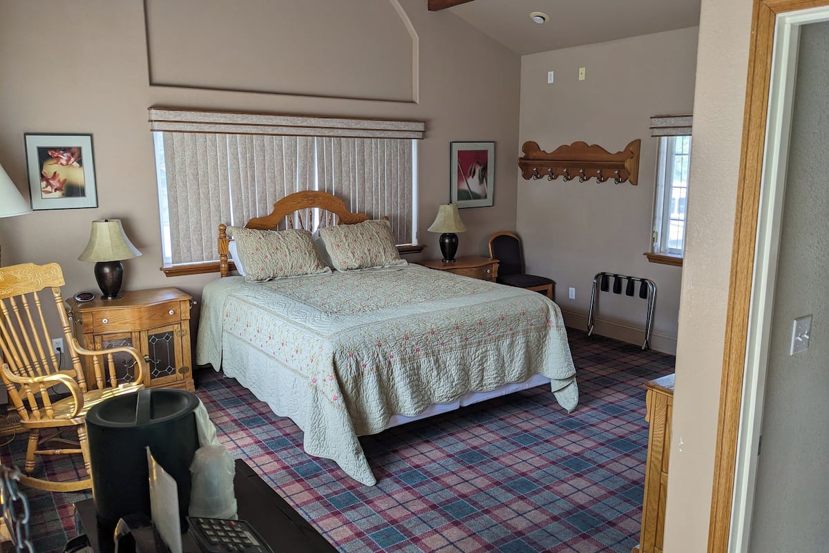 A bedroom with a large bed, a wooden chair, a desk with a lamp, and a radiator.