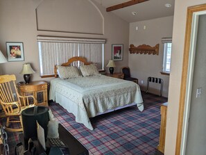 A bedroom with a large bed, a wooden chair, a desk with a lamp, and a radiator.