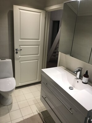 A bathroom with a white toilet, a white sink with a mirror, and a door leading to a staircase.