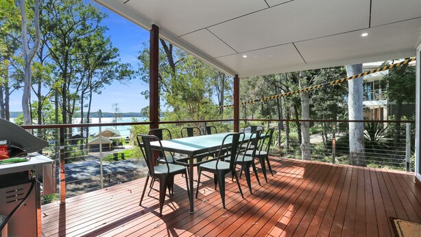 Un espacio de comedor al aire libre techado, con una mesa y sillas, que ofrece vistas panorámicas de árboles y un cuerpo de agua.