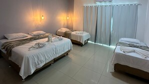 Habitación de hotel con dos camas, un ventanal con cortinas, un equipo de aire acondicionado y luces fijadas a la pared.