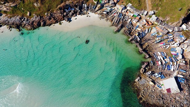 Vista aérea de una zona costera con playa, barcos y un litoral rocoso.