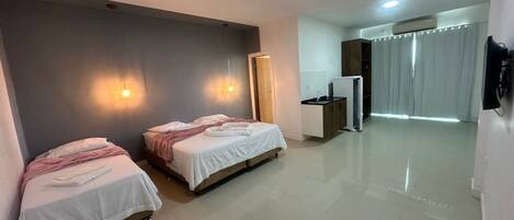 A hotel room with two beds, a kitchenette, a mirror, and a sliding door leading to a balcony.