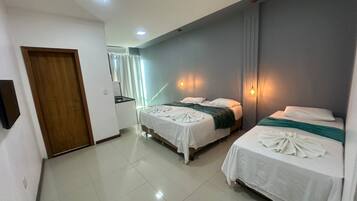 Habitación de hotel con dos camas, un pequeño kitchenette y un baño visible a través de una puerta de vidrio.