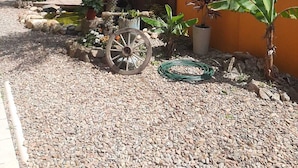A garden with a palm tree, potted plants, a wooden cart, and a yellow wall. - Pousada Vô Lica  (Penha)