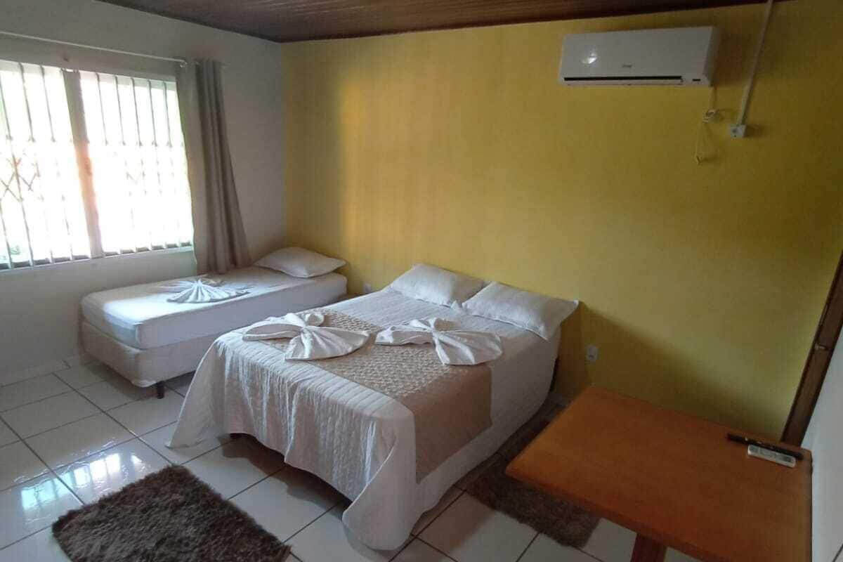 A hotel room with two beds, a small table, a refrigerator, and a window with blinds.