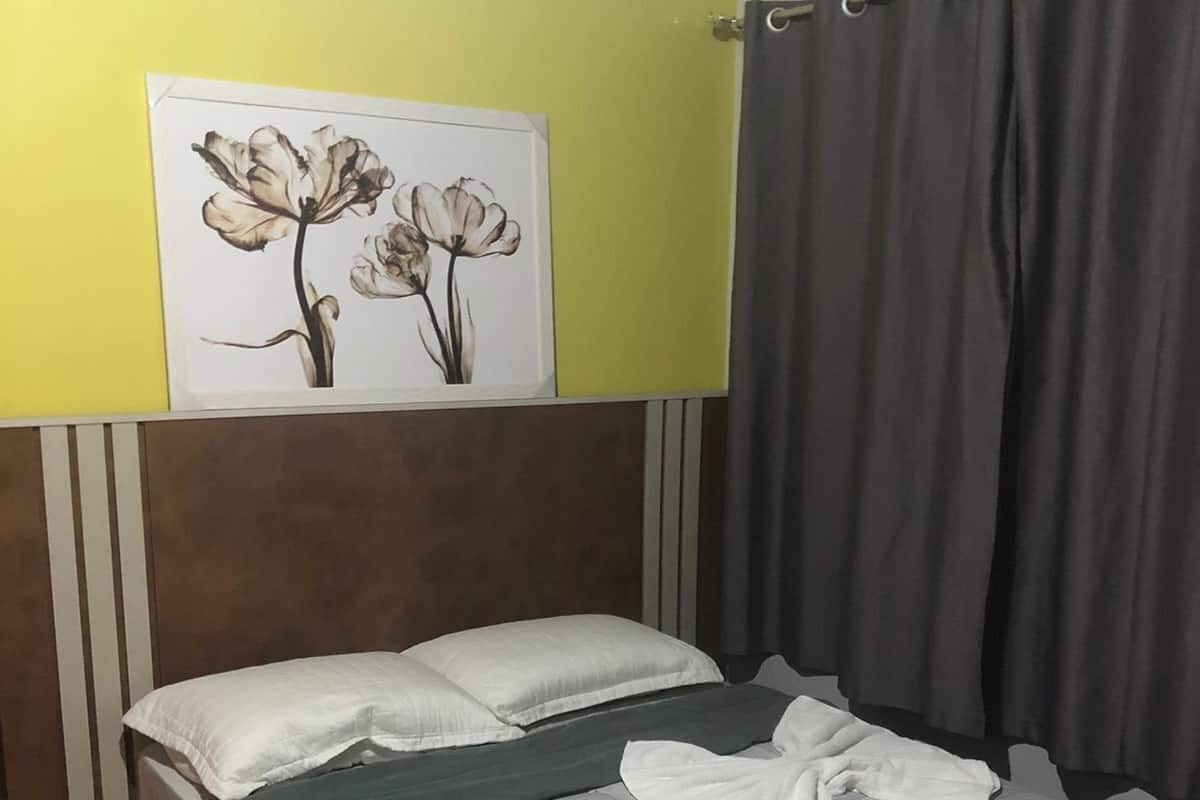 A hotel room with a bed, pillows, a blanket, and a wall-mounted artwork of flowers.