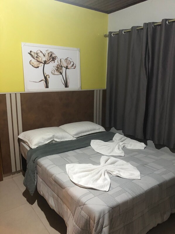 A hotel room with a bed, pillows, a blanket, and a wall-mounted artwork of flowers. - Pousada Vô Lica (Penha)