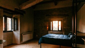 A rustic room with a wooden floor, a bed with a blue bedspread, a radiator, and a window with a view of trees.
