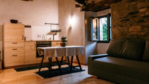 A rustic kitchen with wooden cabinets, a dining table with a cloth, and a stone wall.
