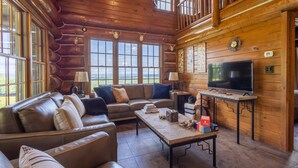 A log cabin interior with a leather sofa, a television, and a fireplace.