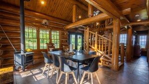 A log cabin interior with a dining area, a fireplace, and a staircase.