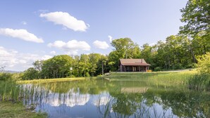 A lodge with a pond in front, surrounded by trees and a clear sky.