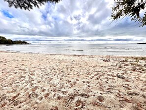 Una playa con huellas en la arena, cielo nublado y una costa distante.