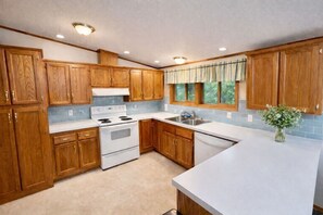 Una cocina con armarios de madera, una estufa blanca, un fregadero y una ventana con cortinas.