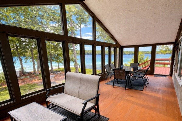 Una habitación amplia con ventanas grandes, una terraza de madera y vistas a un lago.