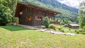 A wooden chalet with a sloped roof, surrounded by a lush green landscape and mountains in the background. - Chalet, 3rd floor, balcony, fireplace or stove, tv, 215m², Morzine (Montriond)