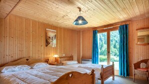 A wooden cabin bedroom with two beds, a nightstand, a lamp, and a chair. - Chalet, 3rd floor, balcony, fireplace or stove, tv, 215m², Morzine (Montriond)