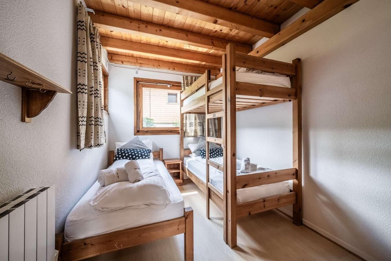 A bunk bed room with wooden beams, a window, and a radiator.