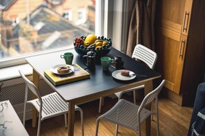 Een eethoek met een tafel gedekt voor twee personen, een schaal fruit, een boek en een koffiepot.