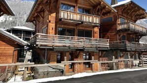 Eine Holzchalet mit mehreren Balkonen und einem in der Ferne sichtbaren Skilift.