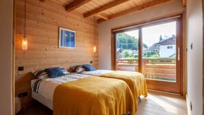 Ein Zimmer mit Holzboden und zwei Betten, einem großen Fenster und Blick auf eine grüne Landschaft.