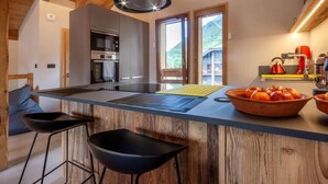 A modern kitchen with a central island, bar stools, and a view of the outdoors.