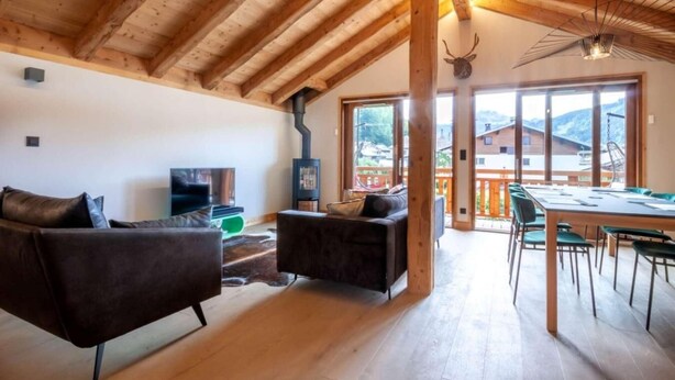 Ein großzügiger Wohnbereich mit Holzbalkendecke, Kamin, Fernseher und Essbereich mit Tisch und Stühlen.