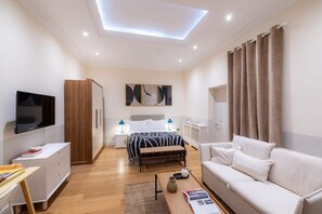 A modern bedroom with a bed, bedside tables, a TV, a wardrobe, and a sofa. - The Courtfield by Nestor - Deluxe Studio (London)