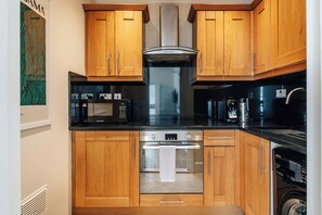 A compact kitchen with wooden cabinets, a microwave, a stove, and a coffee maker. - The Courtfield - Studio Apartment in Kensington (London)