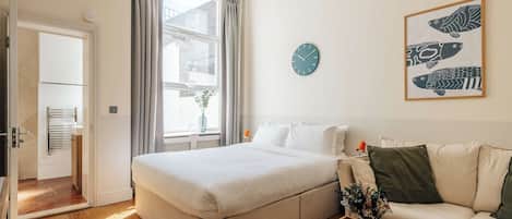 Une chambre d’hôtel moderne avec un grand lit, un canapé, une petite table et une horloge murale.