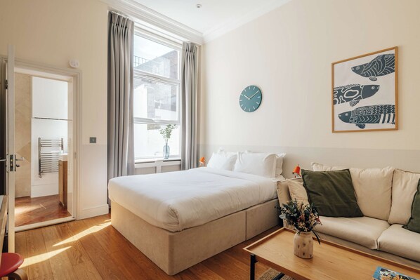 Une chambre d’hôtel moderne avec un grand lit, un canapé, une petite table et une horloge murale.