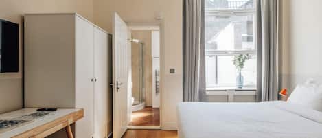 A hotel room with a bed, a desk, a chair, a wardrobe, and a window with curtains.