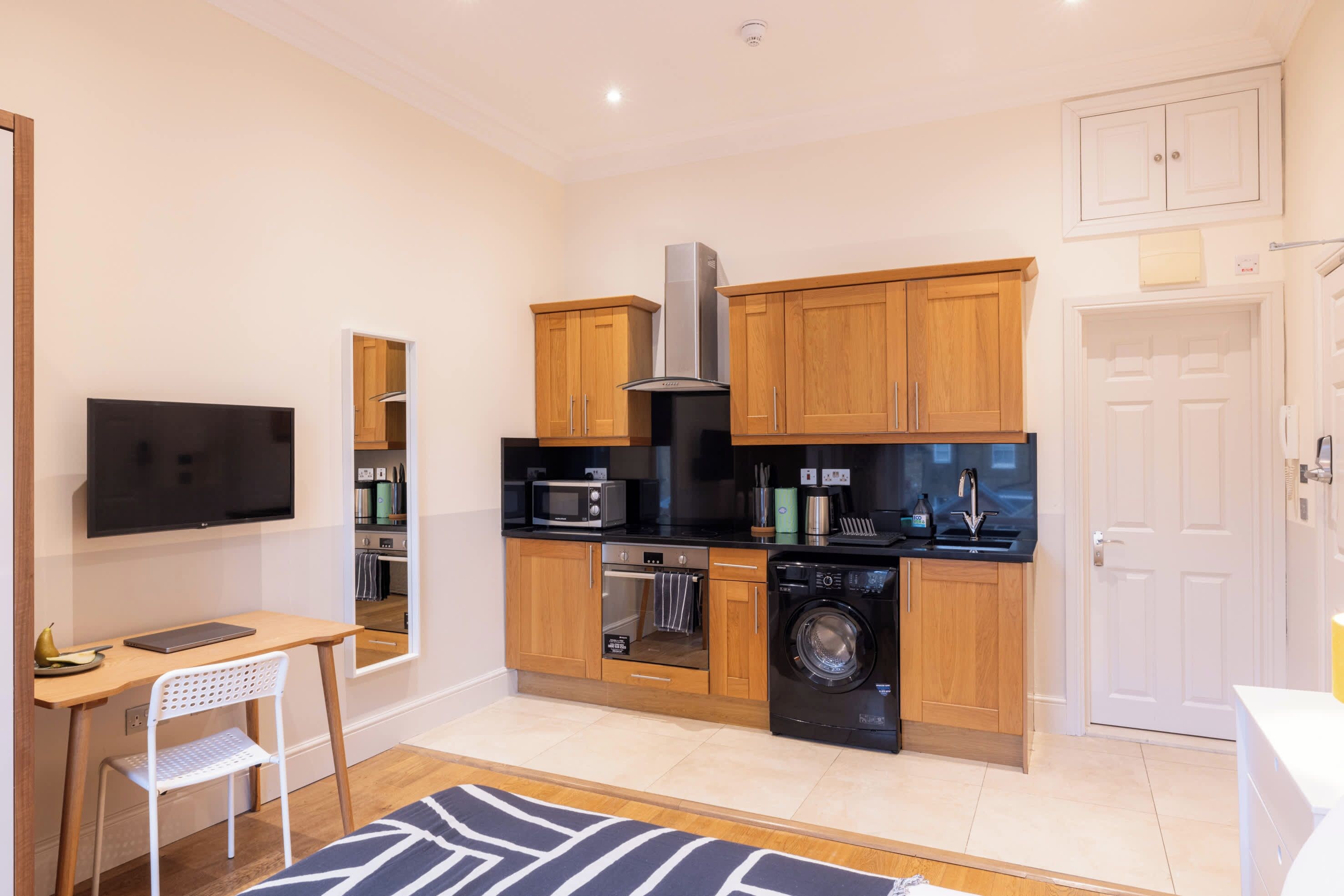 A compact kitchen with wooden cabinets, a microwave, oven, and washing machine.
