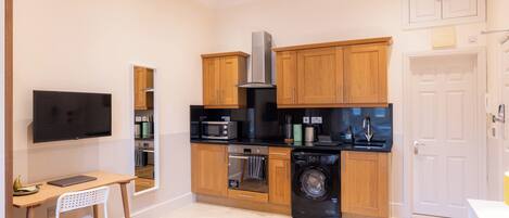 A compact kitchen with wooden cabinets, a microwave, oven, and washing machine.