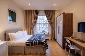 Une chambre d’hôtel avec un lit, un bureau, une chaise, une télévision et une fenêtre avec des rideaux.