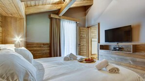 Habitación de hotel con techo de madera, cama con sábanas blancas, televisor de pantalla plana y bandeja de desayuno sobre la cama.
