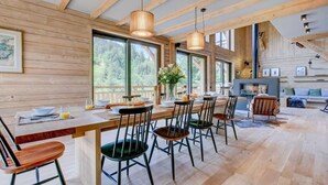 Un comedor amplio con una larga mesa de madera, numerosas sillas y ventanas grandes que ofrecen vistas al exterior.