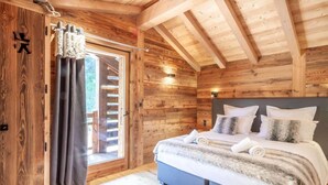 A wooden cabin bedroom with a bed, curtains, and a window. - Chalet, swimming pool, sauna, terrace, fireplace or stove, parking, tv, ski locker, 175m², Morzine (Morzine)