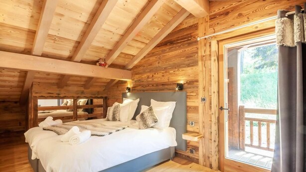 A cozy wooden cabin bedroom with a large bed, a window with curtains, and a view of greenery outside. - Chalet, swimming pool, sauna, terrace, fireplace or stove, parking, tv, ski locker, 175m², Morzine (Morzine)