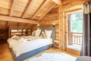 A cozy wooden cabin bedroom with a large bed, a window with curtains, and a view of greenery outside. - Chalet, swimming pool, sauna, terrace, fireplace or stove, parking, tv, ski locker, 175m², Morzine (Morzine)