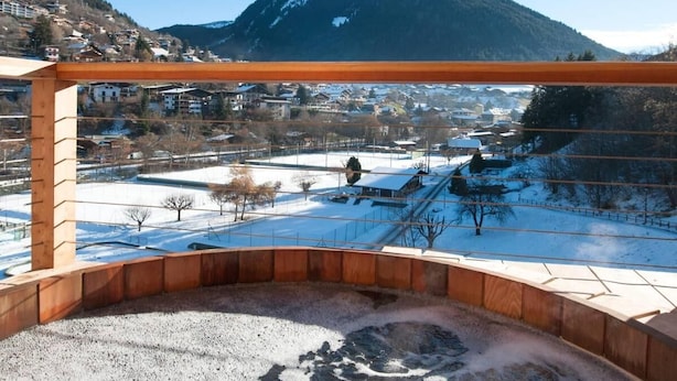 A view from a balcony with a wooden railing, overlooking a snowy landscape with houses and a mountain in the background. - Chalet, 70m from ski lifts, view mountain, swimming pool, sauna, fireplace or stove, parking, tv (Morzine)