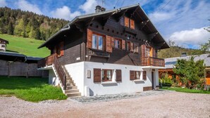 A two-story wooden house with a balcony, a staircase leading to the upper floor, and a gravel driveway.