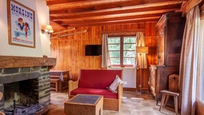 A cozy cabin interior with a stone fireplace, wooden walls, a red sofa, and a television.